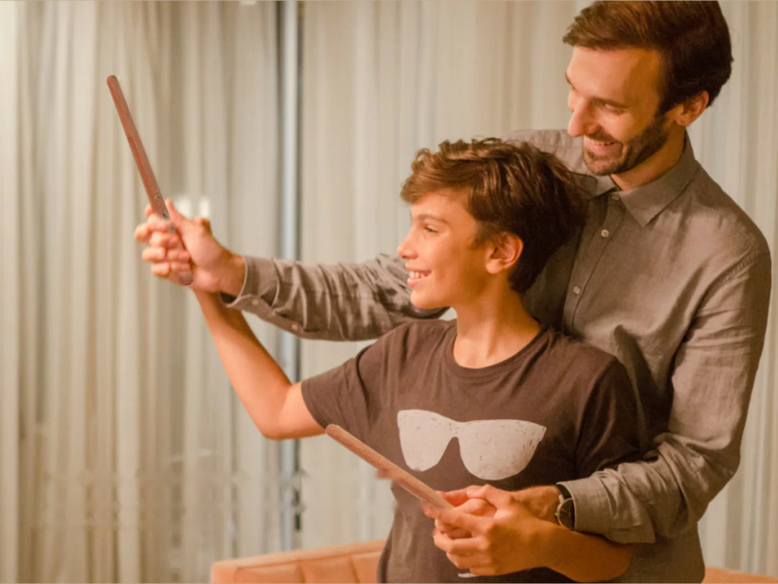 Vader en zoon drummen samen in de lucht met PocketDrum-sticks in de woonkamer, in warm avondlicht